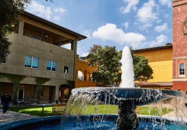 A water fountain in the foreground of a picture showing two DreamWorks buildings with people walking and sitting between them.
