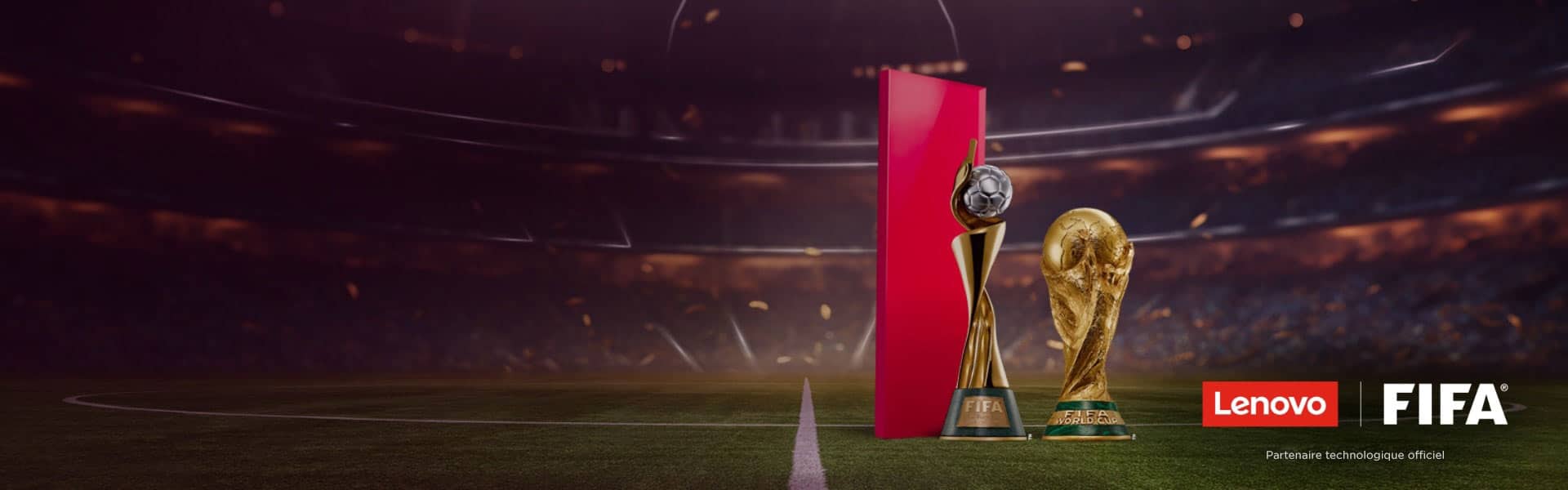 Un terrain de soccer où la foule est brouillée du stade, le trophée de la Coupe du monde de la FIFA, la structure rouge avec ballon de soccer au-dessus, les logos Lenovo et de la FIFA, et